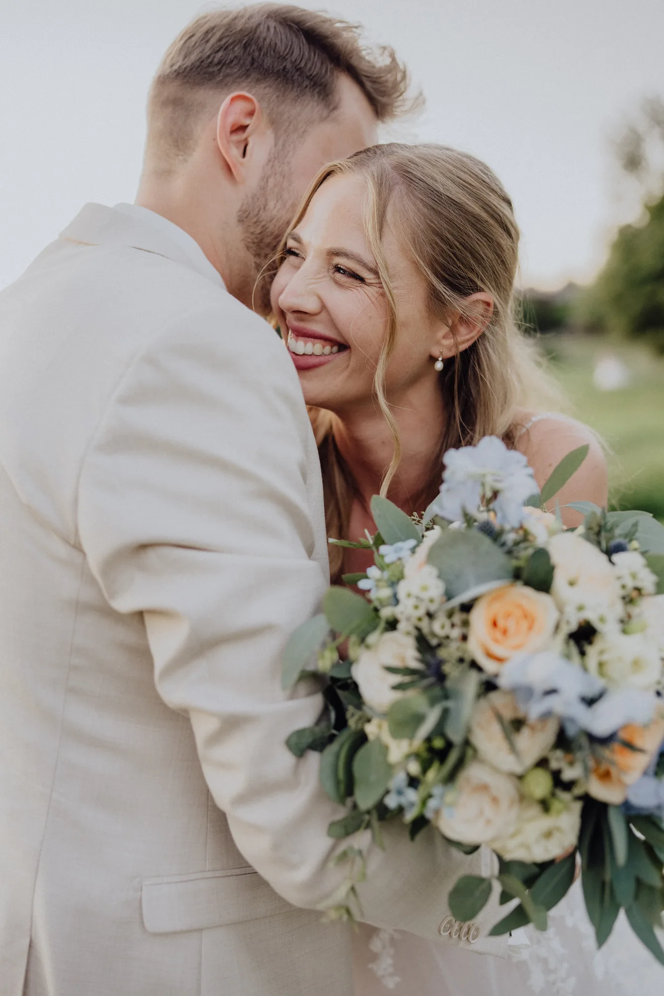 Anna lacht an Joosts Schulter, mit Brautstrauß – Hochzeit Anna & Joost, Romantik Hotel Fuchsbau, Timmendorfer Strand
