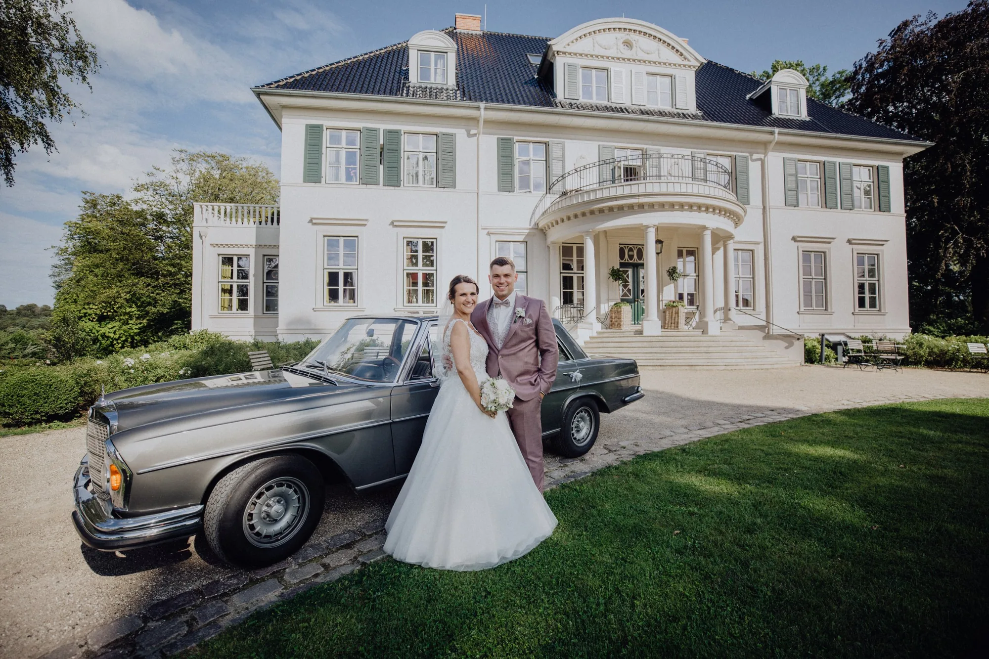 Bella und Tom mit einem Mercedes-Oldtimer vor dem Herrenhaus – Hochzeit Bella & Tom, Gut Immenhof, Malente
