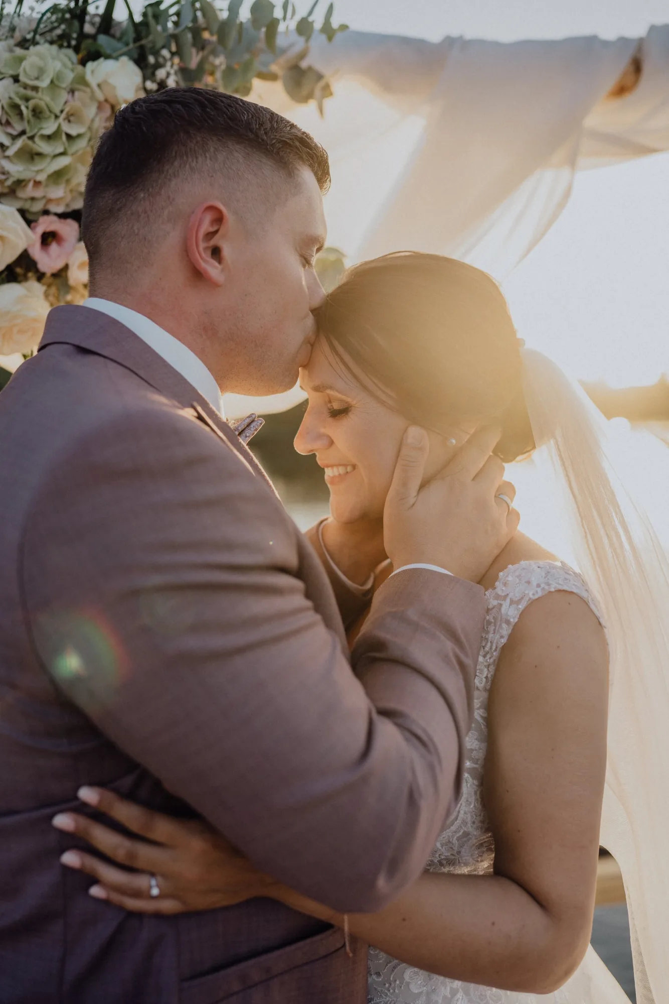 Tom küsst Bella im Gegenlicht der Abendsonne auf die Stirn – Hochzeit Bella & Tom, Gut Immenhof, Malente