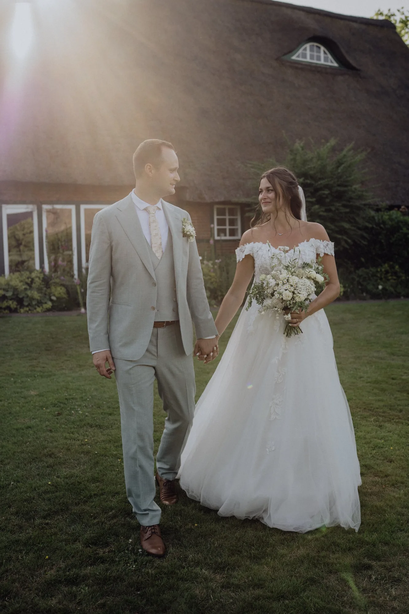 Franzi und Tim gehen Hand in Hand über die Wiese vor der Reetdachscheune – Hochzeit Franzi & Tim, De Ole Schüün, Hüttblek