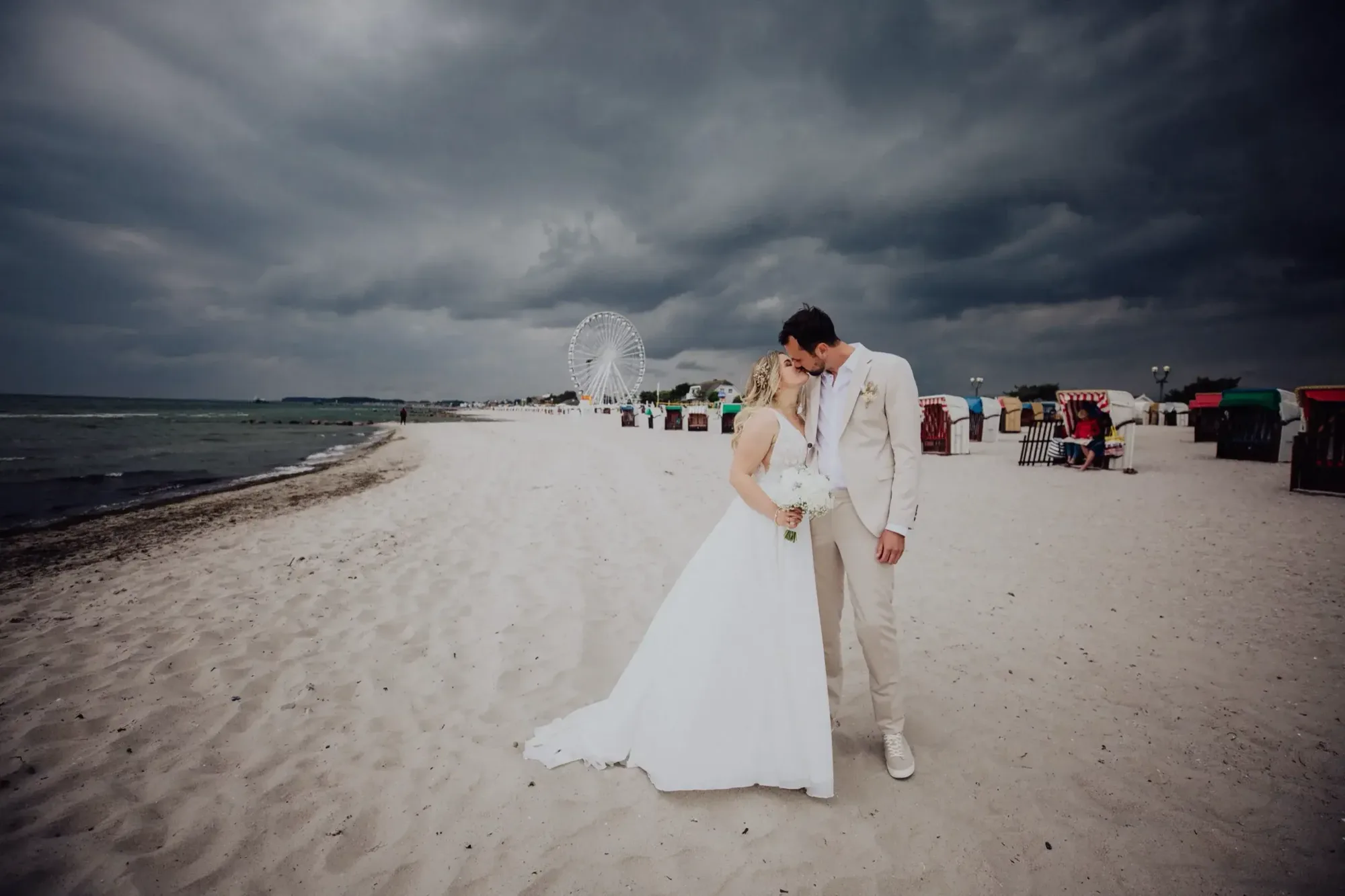 Brautpaar am Strand, im Hintergrund Strandkörbe unter dunklen Wolken