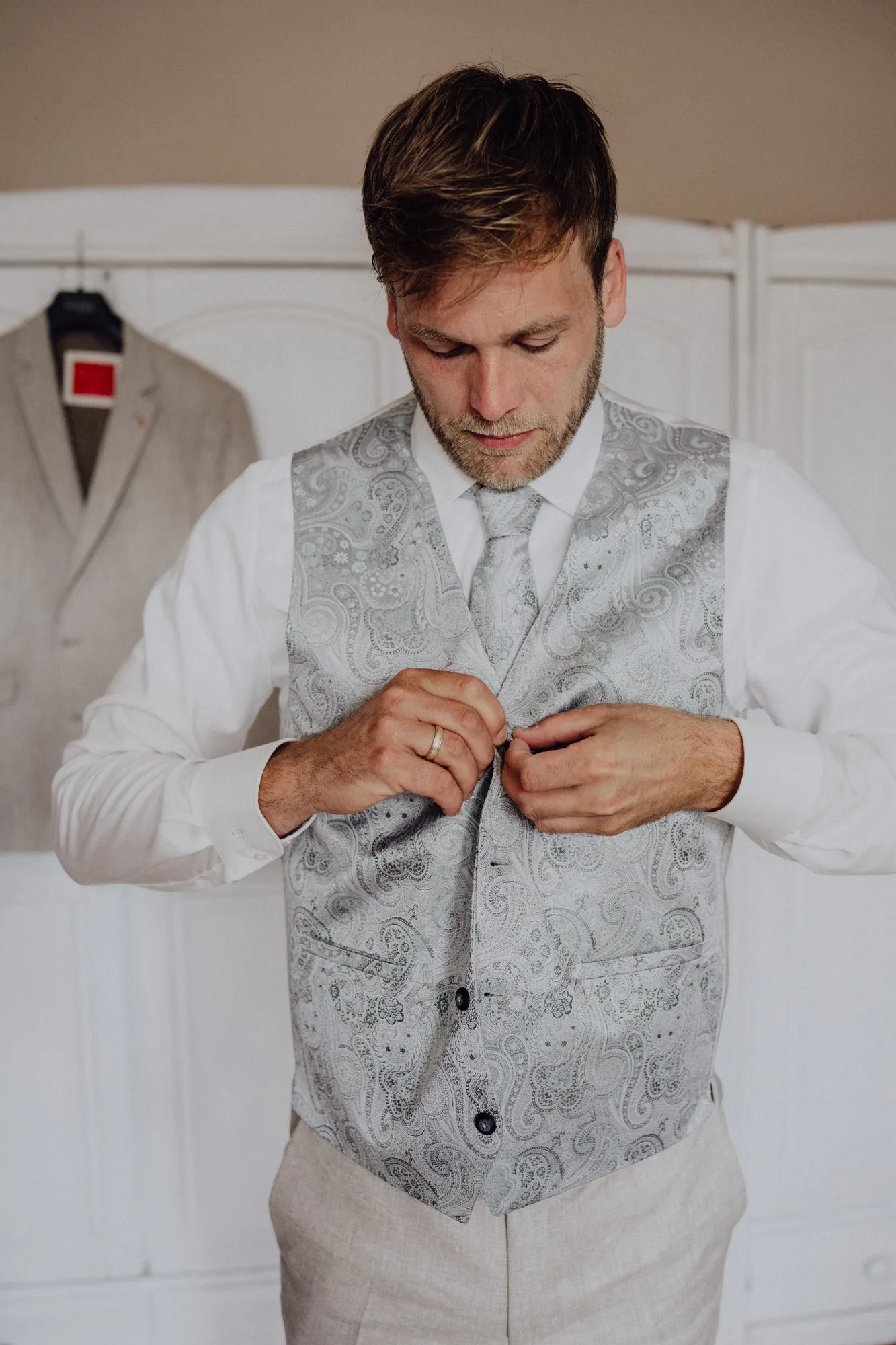 Jannik schließt die Knöpfe seiner Paisley-Weste – Hochzeit Maria & Jannik, Gut Pronstorf
